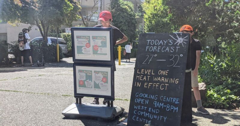 Two neighbours read a sign sharing information and resources about extreme heat and the weather forecast in Vancouver’s West End.