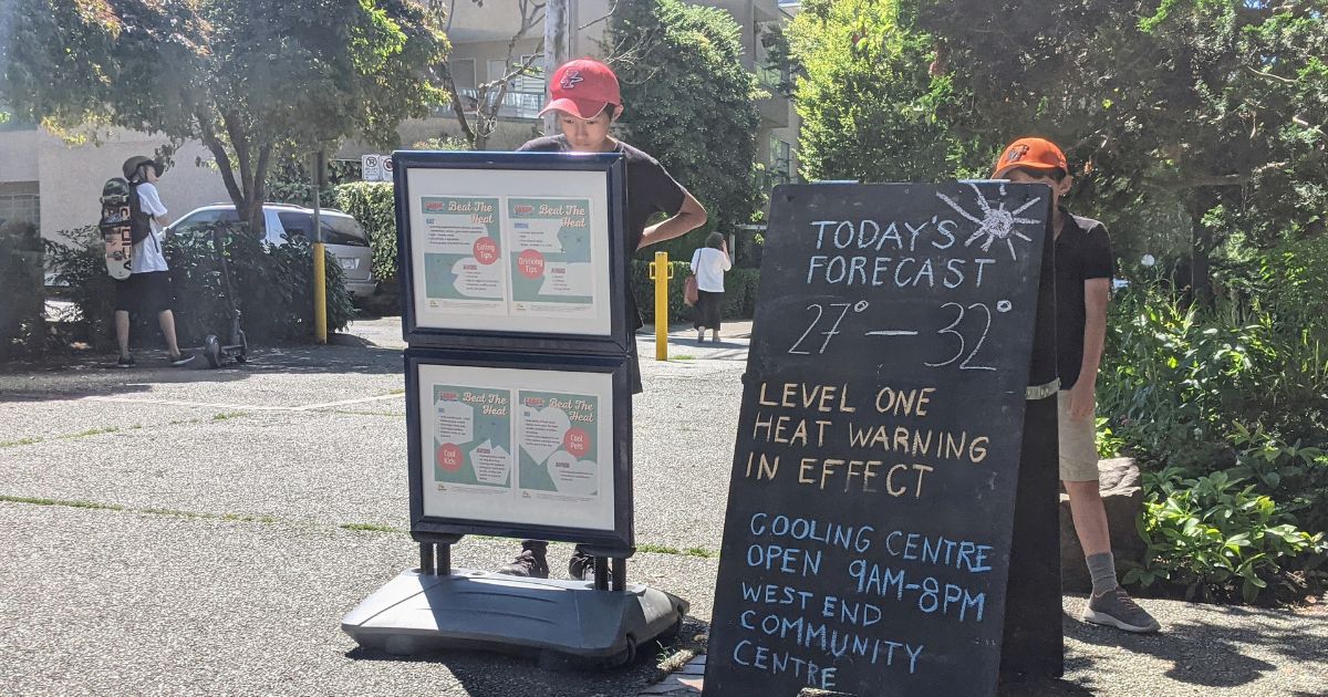 Two neighbours read a sign sharing information and resources about extreme heat and the weather forecast in Vancouver’s West End.